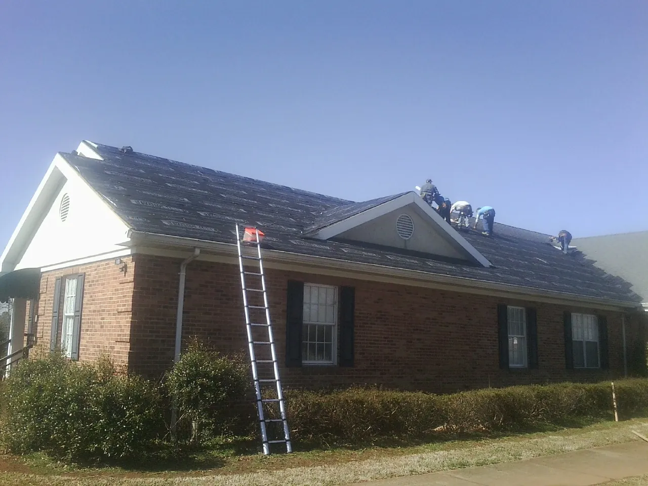 Crew tearing shingles off a brick ranch roof with a ladder set — Metal Roof Repair work by our crew in Storrs Mansfield