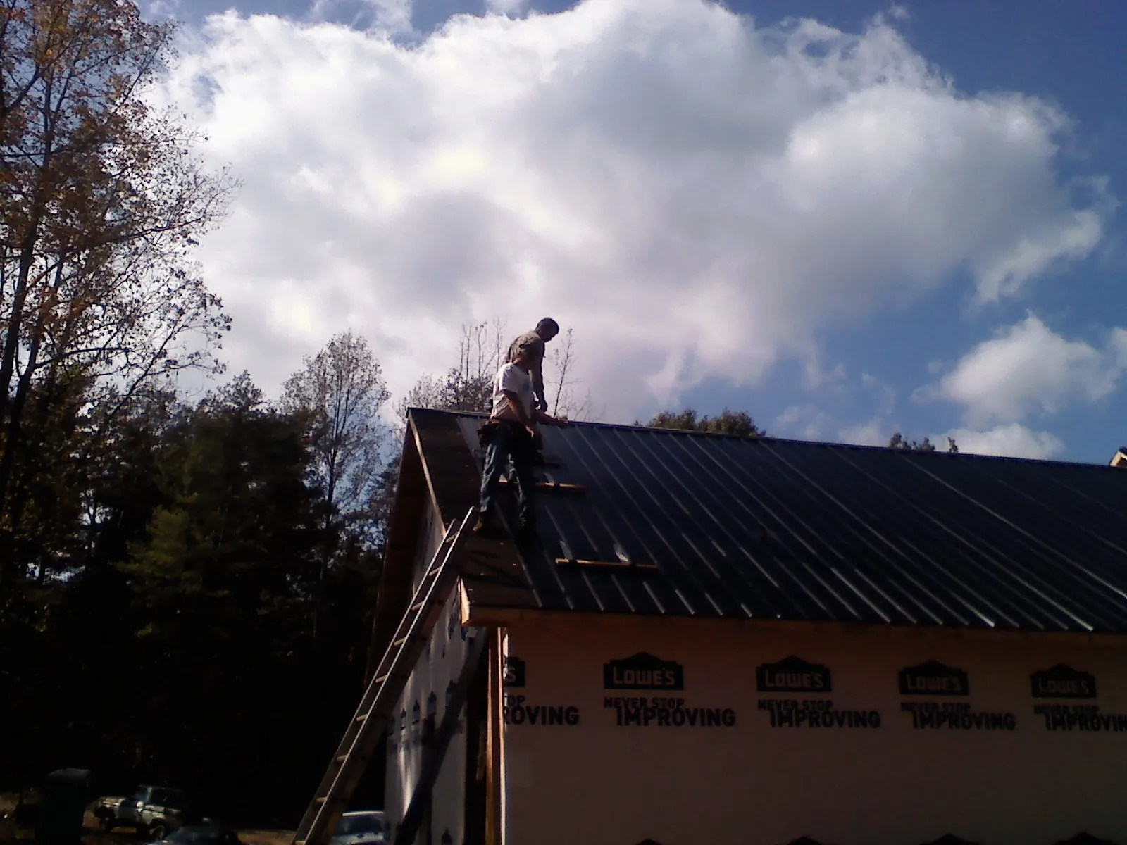 Roofer fastening dark metal panels high against a cloudy sky, from a Roof Inspection job in Storrs Mansfield