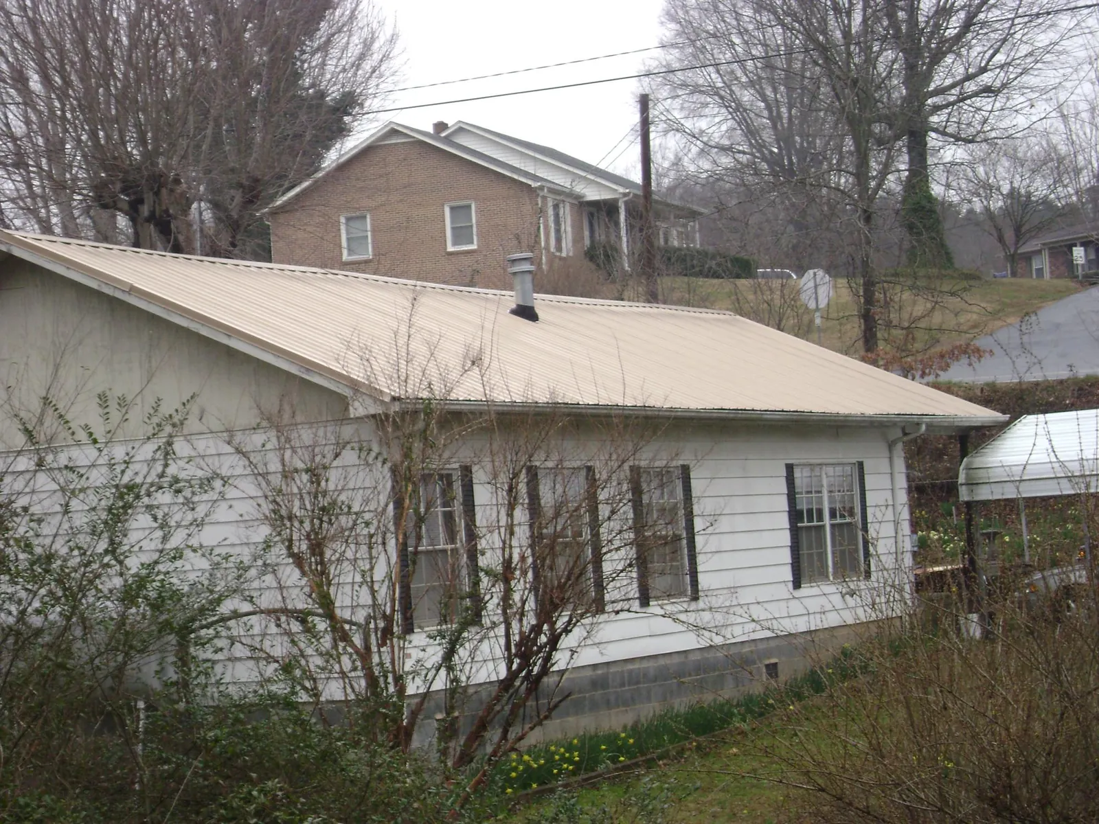 Tan metal roof on a white sided house set into a hillside — Commercial Roofing by Roofing Brothers in Storrs Mansfield